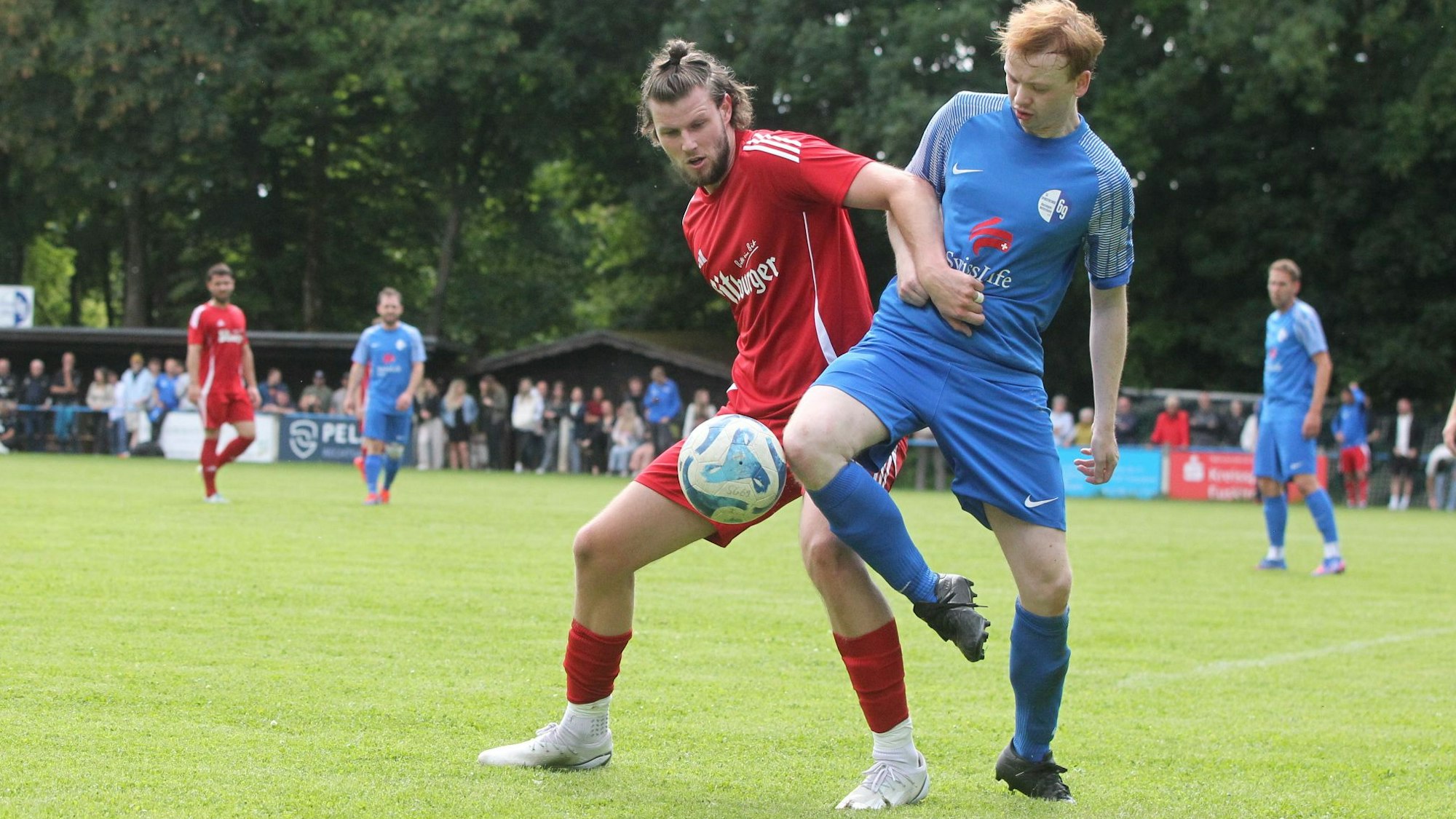 Zwei Fußballer kämpfen auf einem Kunstrasenplatz um den Ball. Der eine hält den anderen am Trikot fest.