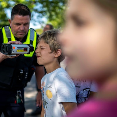 Das Bild zeigt einen Schüler, der mithilfe eines Polizisten durch ein Lasergerät schaut.