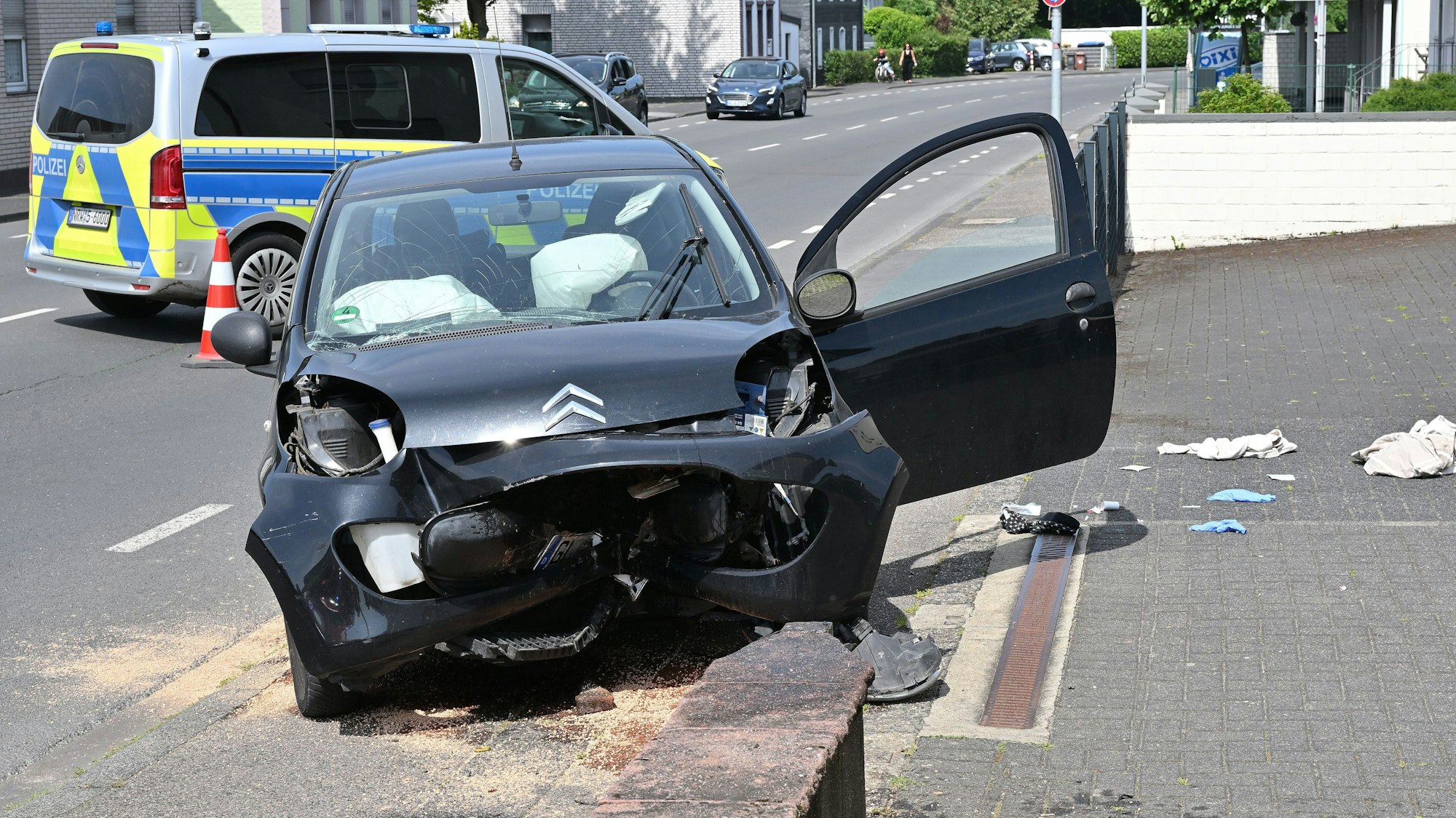 Ein Auto ist frontal gegen eine Mauer gefahren. Im Hintergrund ist ein Polizeifahrzeug zu sehen.