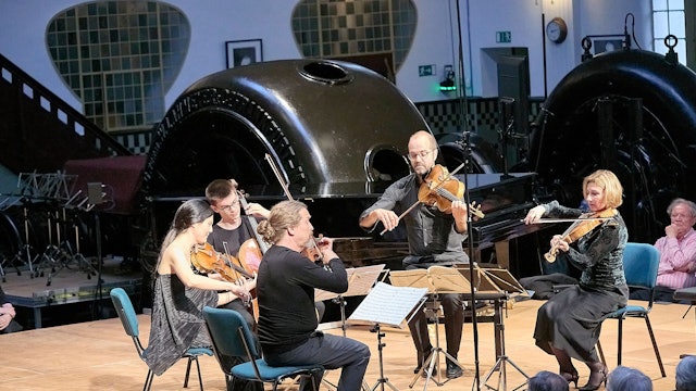 Zwei Musikerinnen und drei Musiker sitzen mit ihren Streichinstrumenten auf der Bühne des Jugendstilkraftwerks in Heimbach.