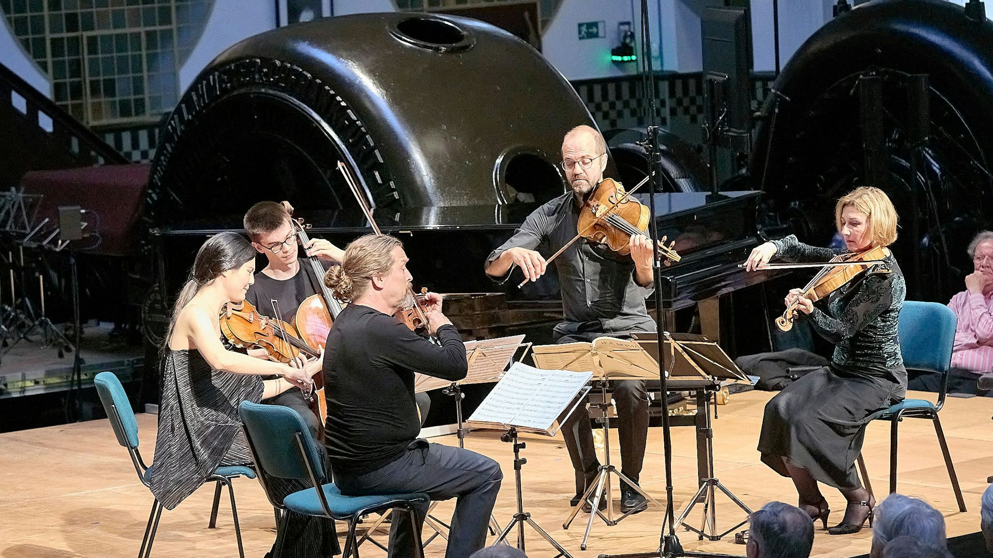 Zwei Musikerinnen und drei Musiker sitzen mit ihren Streichinstrumenten auf der Bühne des Jugendstilkraftwerks in Heimbach.
