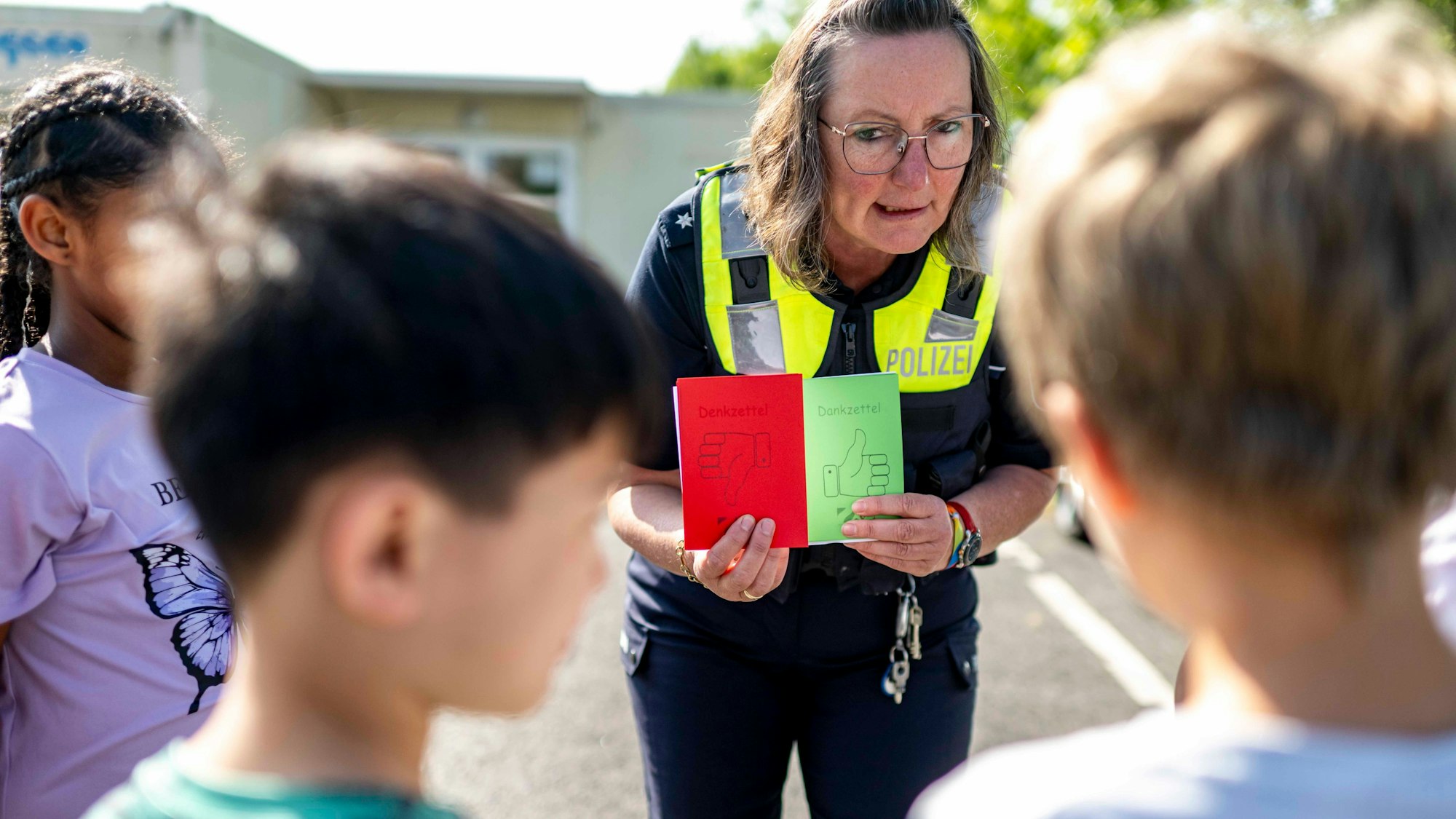 Das Bild zeigt eine Polizeibeamtin, die Kindern einen roten und einen Zettel zeigt.
