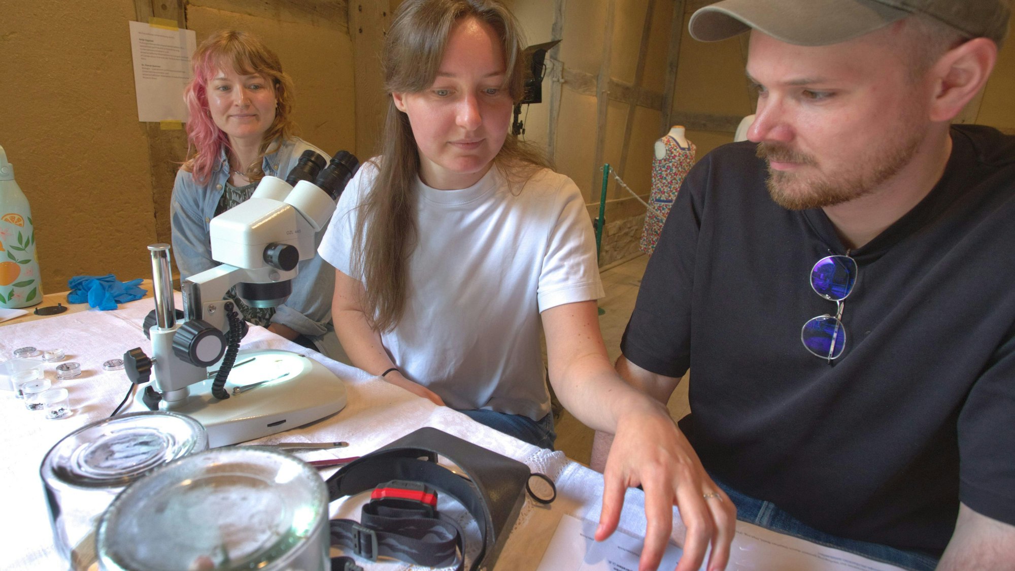 Katja Schüller zeigt Isabelle Houben und Martin Schinken unter dem Mikroskop kleine Tierchen, die mit Stoff zu tun haben.