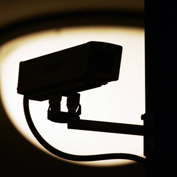 Eine Video-Überwachungskamera zeichnet sich vor einer Lampe als dunkle Silhouette ab