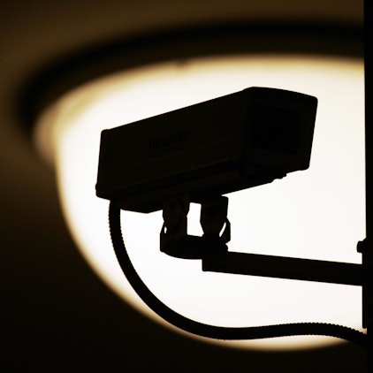 Eine Video-Überwachungskamera zeichnet sich vor einer Lampe als dunkle Silhouette ab