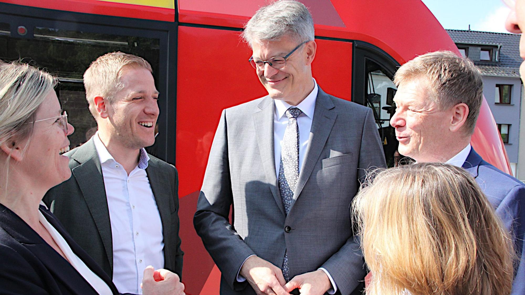 Eine Gruppe von Personen steht vor einem roten Vareo-Triebwagen, sie unterhalten sich miteinander und lachen.