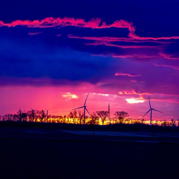Ein Gewitter im Sonnenuntergang über dem Rhein-Erft-Kreis/Kreis Euskirchen. Im Sonnenuntergang drehen sich am Horizont Windräder.