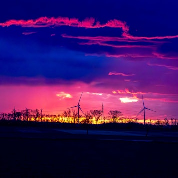 Ein Gewitter im Sonnenuntergang über dem Rhein-Erft-Kreis/Kreis Euskirchen. Im Sonnenuntergang drehen sich am Horizont Windräder.