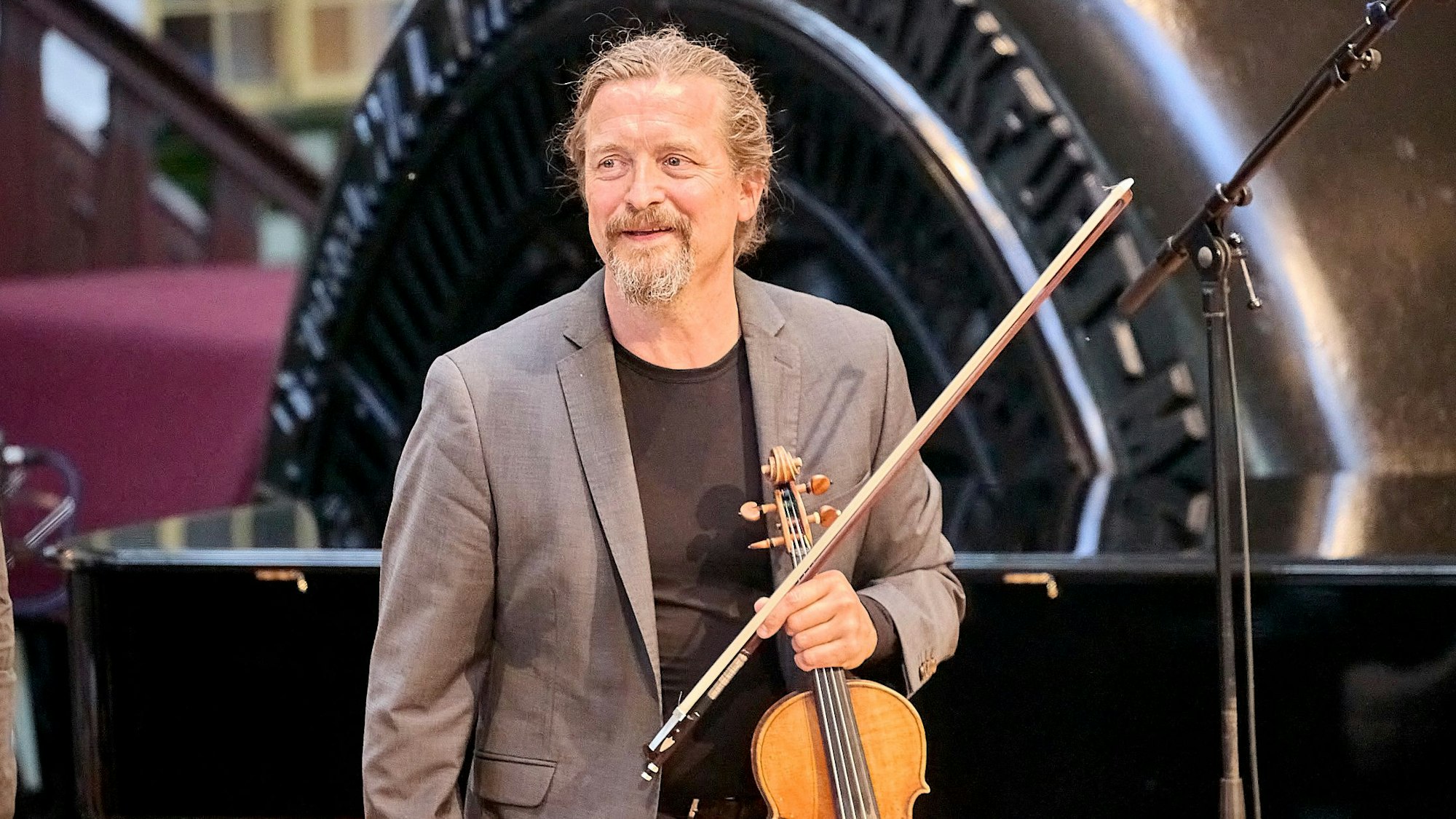 Christian Tetzlaff hält seine Geige in der linken Hand. Im Hintergrund sind Anlagen des RWE-Kraftwerks in Heimbach zu sehen.