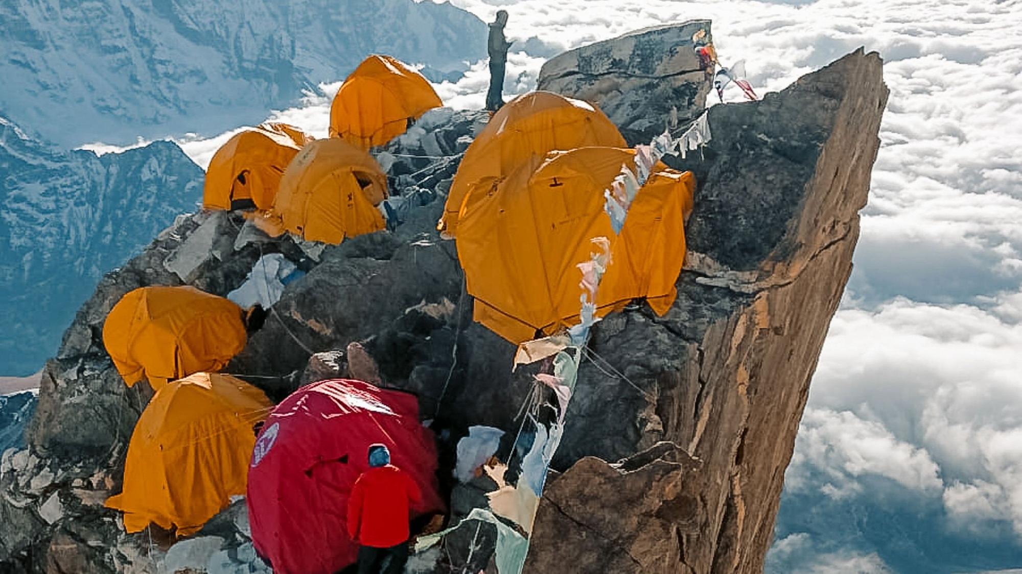 Auf einem Bergvorsprung stehen mehrere Zelte, dazwischen zwei Personen.