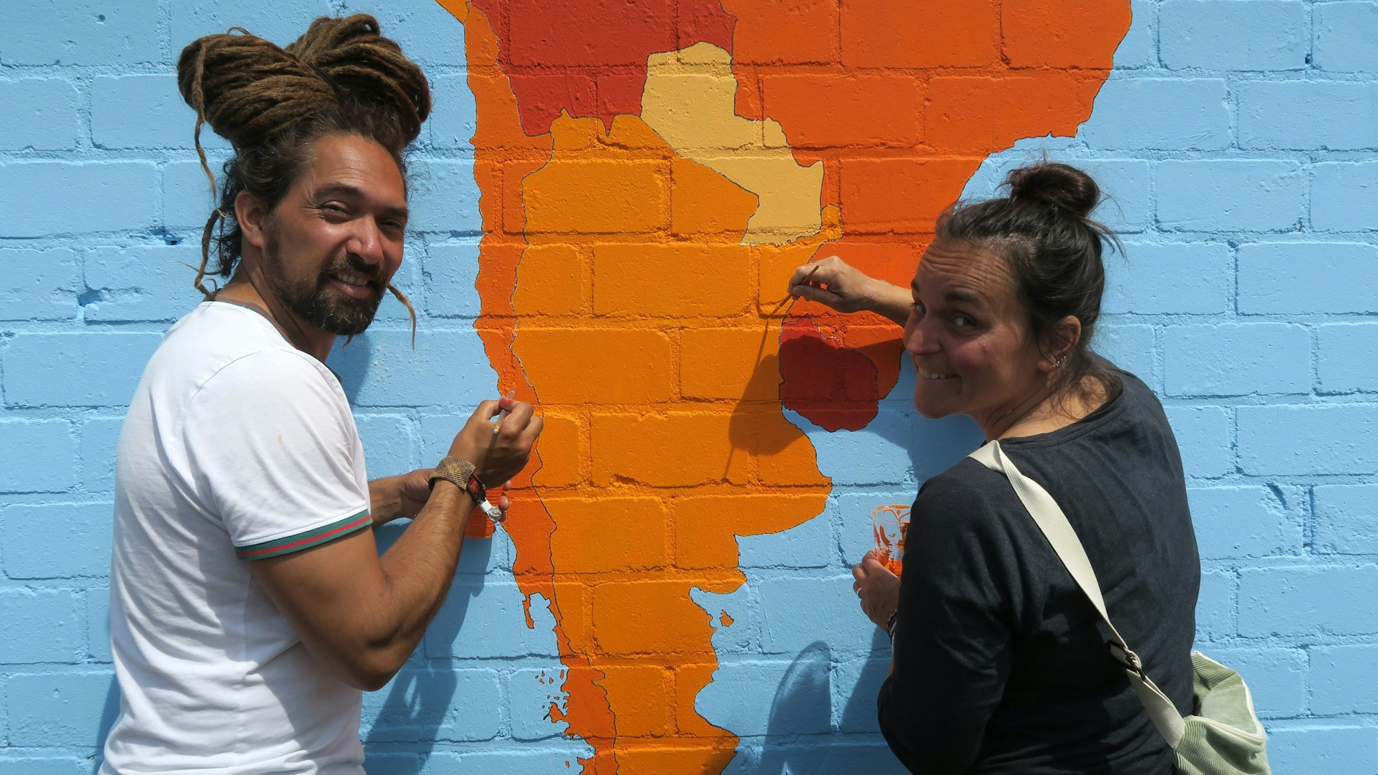 Ein Mann und eine Frau sind dabei, mit einem Pinsel den Kontinent Südamerika auszumalen, der riesig auf einer Mauer prangt.