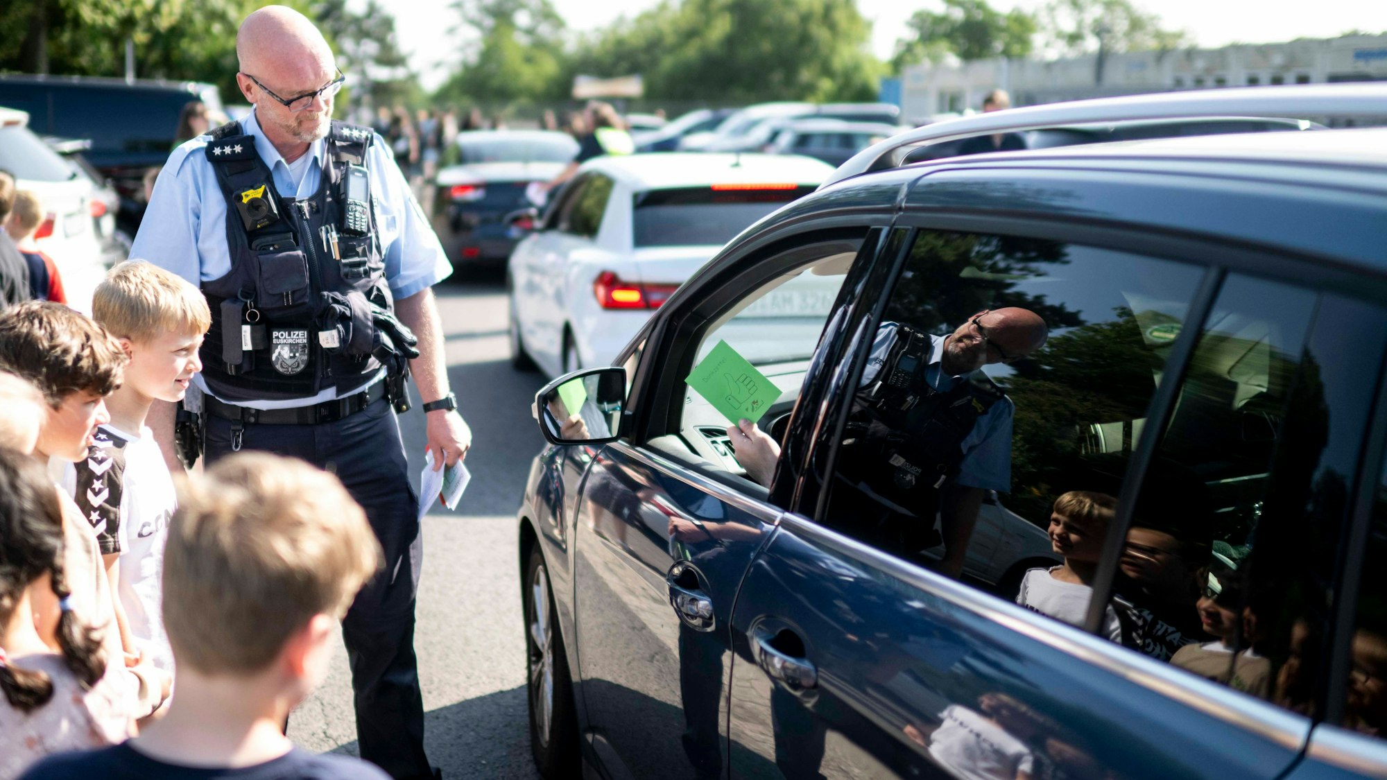 Das Bild zeigt einen Polizeibeamten, der mit Kindern an der Seite eines Autos steht.