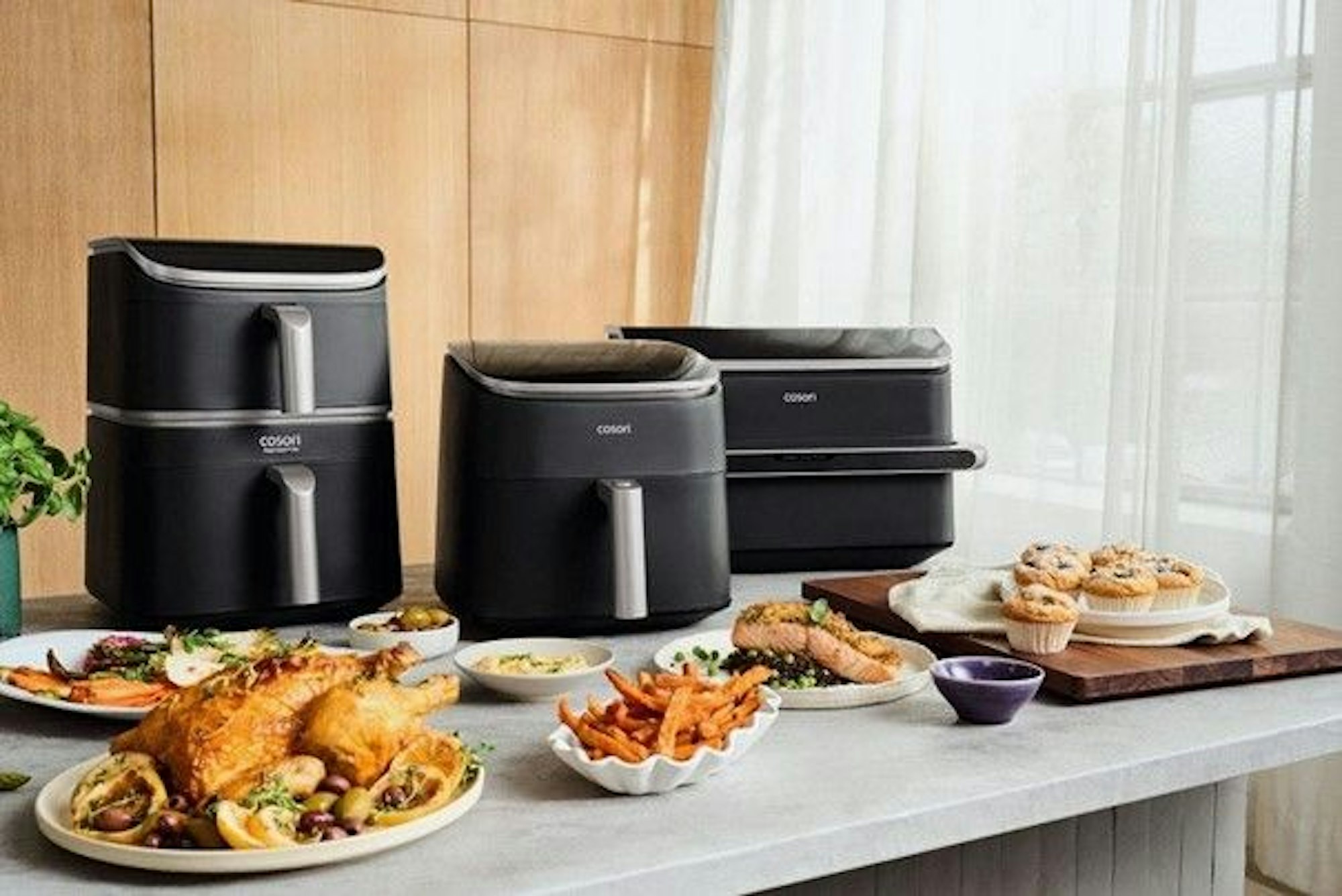 Cosori Heißluftfritteusen Turbo-Serie auf einem Tisch mit mehreren Speisen.