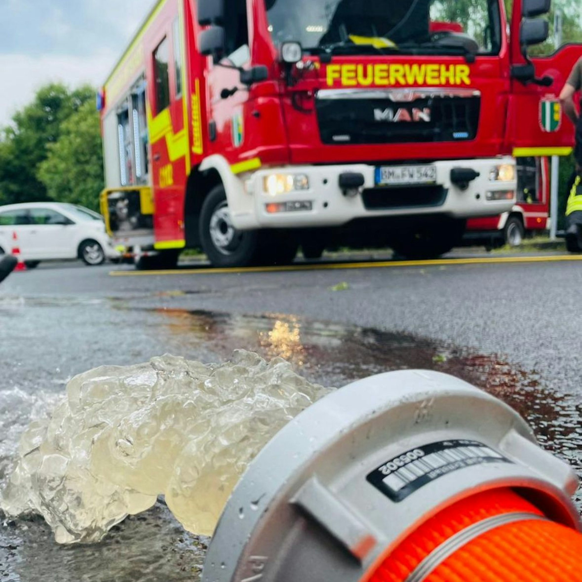 Aus einem Feuerwehrschlauch läuft Wasser auf eine Straße, im Hintergrund steht ein Einsatzwagen.