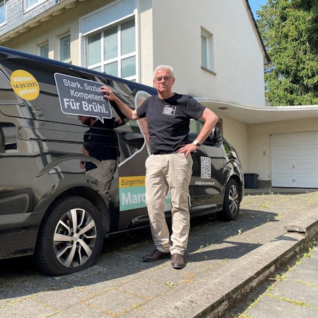 Zu sehen ist Marc Prokop vor dem Kleinbus, dessen Reifen platt sind.