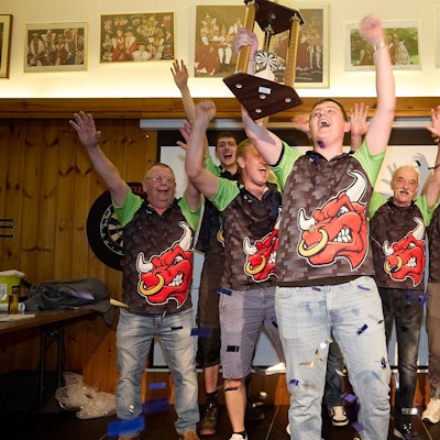 Sieben Männer reißen die Arme hoch, einer hält einen Pokal, einer anderer eine Urkunde in die Luft.