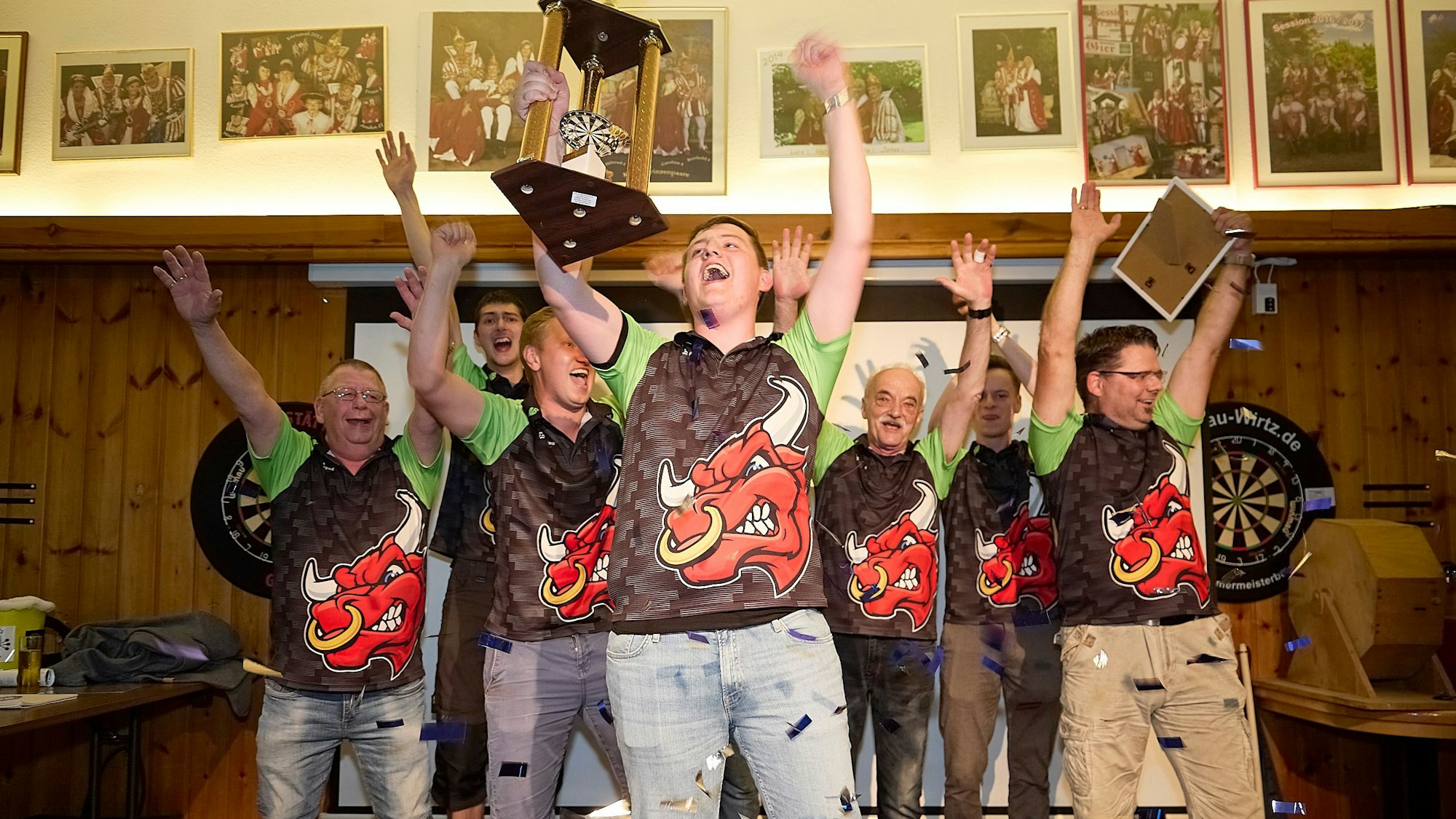 Sieben Männer reißen die Arme hoch, einer hält einen Pokal, einer anderer eine Urkunde in die Luft.