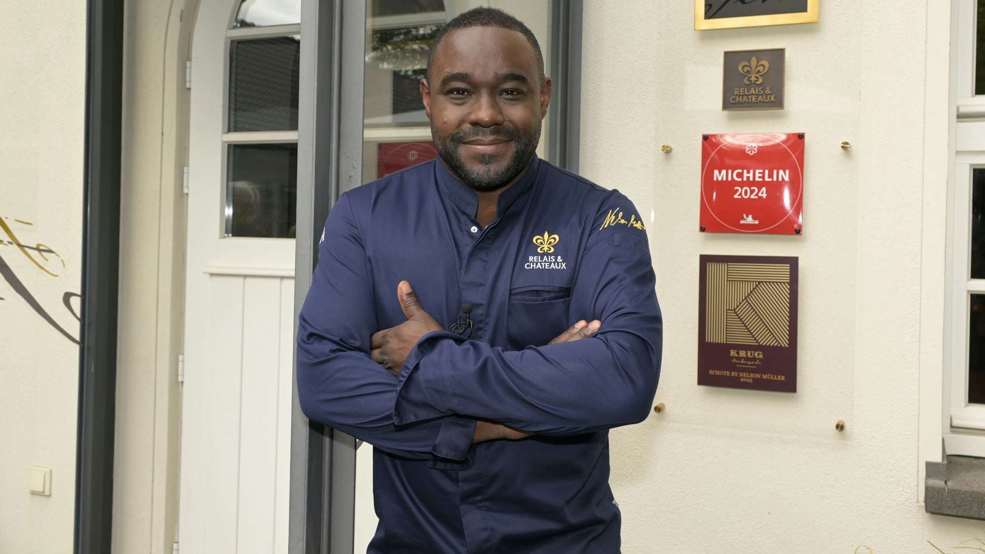 Nelson Müller steht vor der Schote, an der eine Plakette mit der Aufschrift „Michelin 2024“.