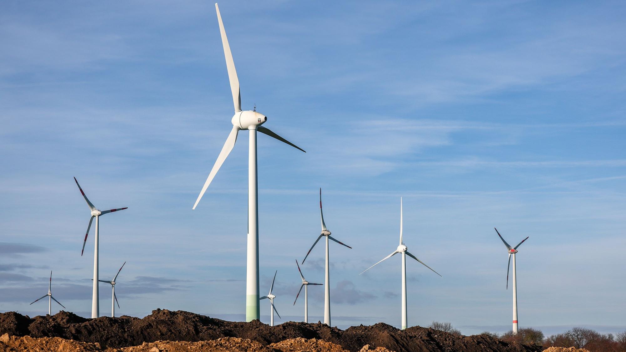 Windräder stehen hinter Erdhaufen am Rande eines Baufeldes.