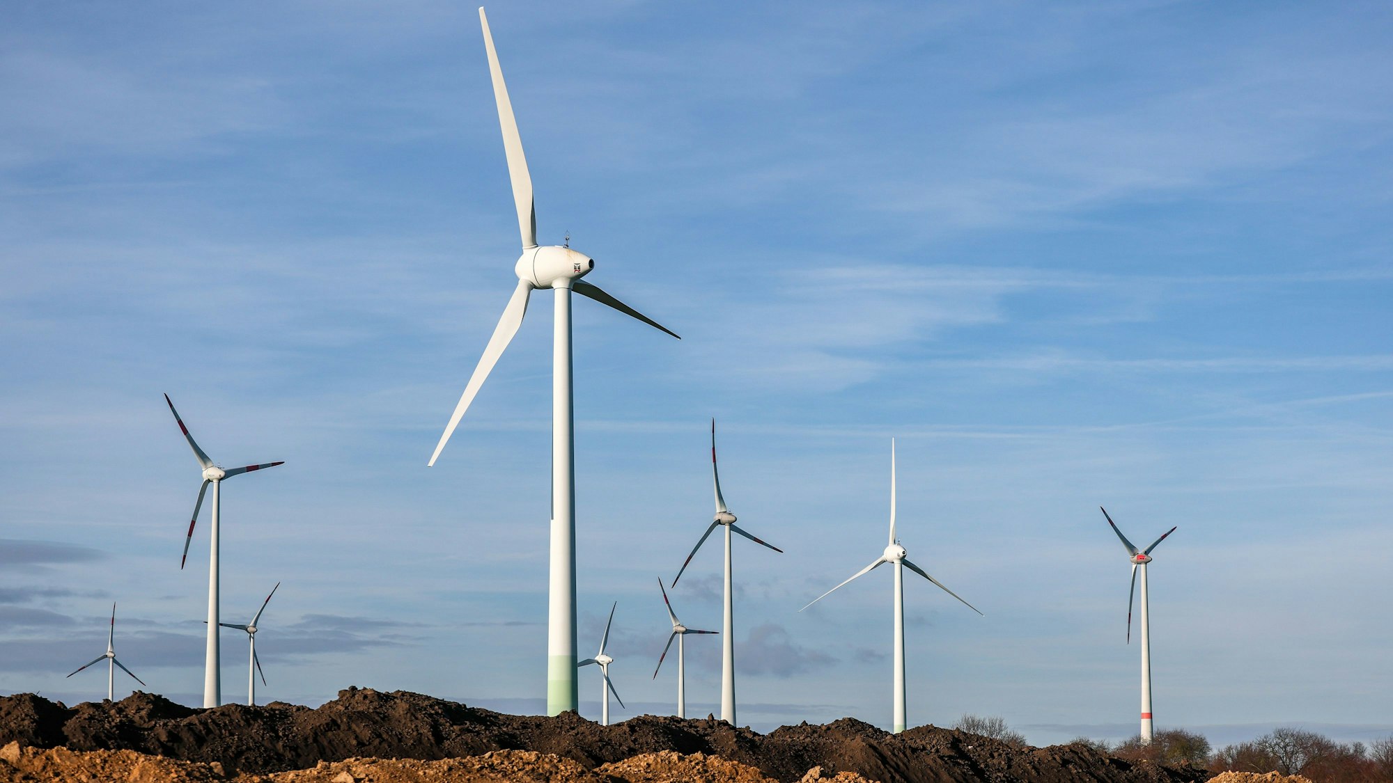 Windräder stehen hinter Erdhaufen am Rande eines Baufeldes.