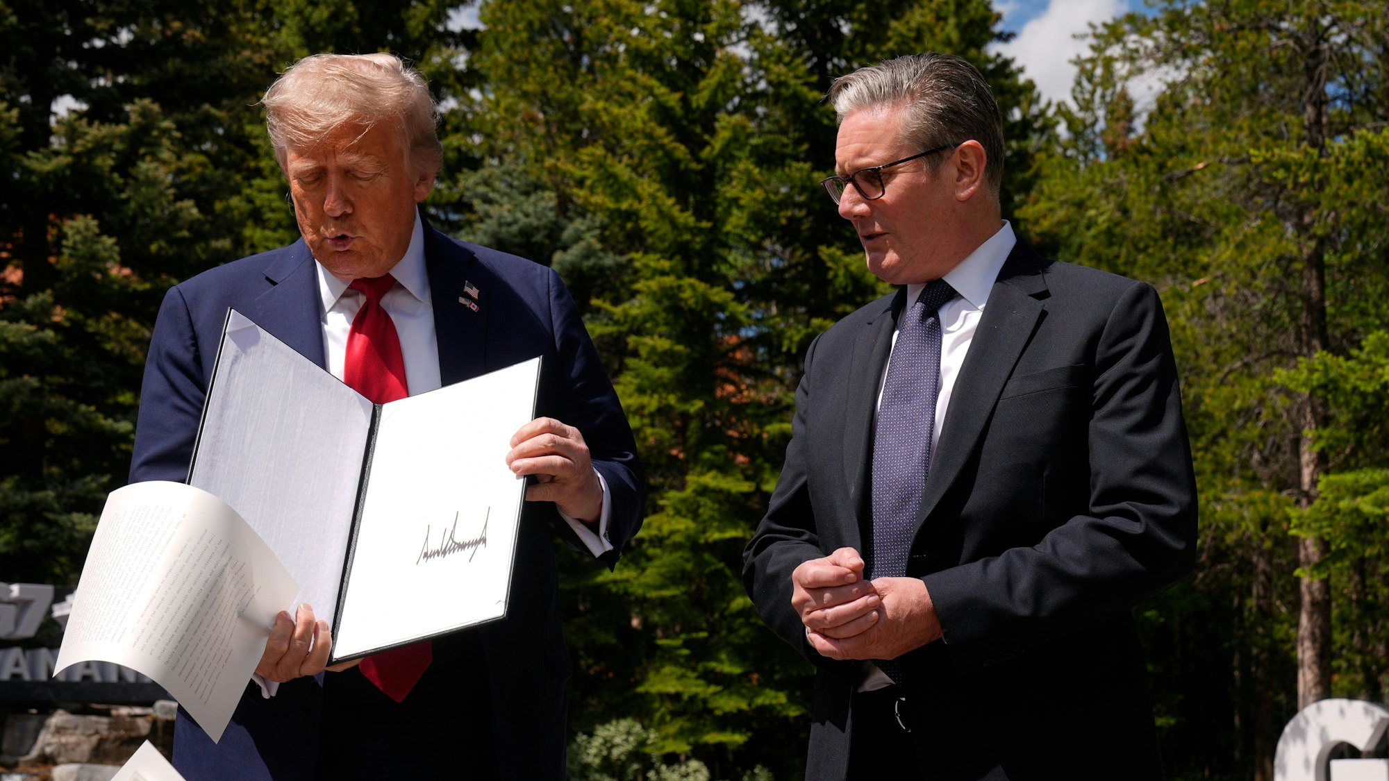 US-Präsident Donald Trump lässt Papiere fallen, als er am Rande des G7-Gipfels mit dem britischen Premierminister Keir Starmer zusammentrifft.