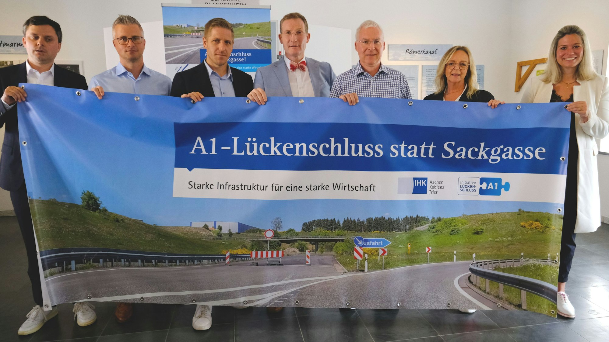 IHK-Aktion zum A1-Lückenschluss, ein entsprechendes Transparent halten v.l.n.r.): Philipp Piecha (IHK Aachen), Daniel Claßen (Spedition Berners), Markus Ramers, Michael F. Bayer (IHK Aachen), Stephan Mahlert (Pappen Olef GmbH), Sabine Preiser-Marian (Bürgermeisterin Bad Münstereifel), Jennifer Meuren (Bürgermeisterin Blankenheim).