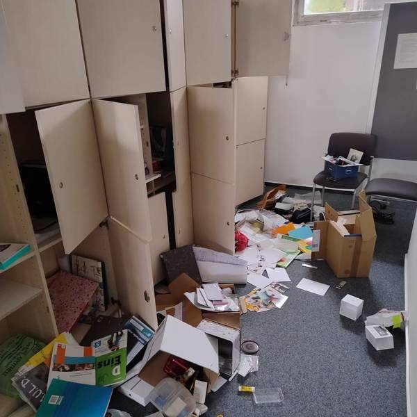 Ordner, Papier, Bücher, Kartons liegen verteilt auf dem Boden des Schulraums. Schranktüren stehen offen.