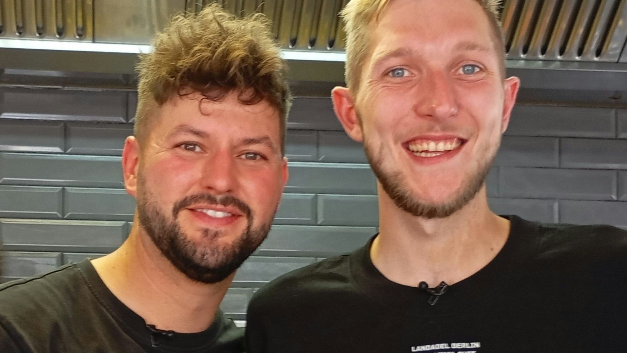 Auf dem Bild sind zwei junge Männer in schwarzen T-Shirts zu sehen.