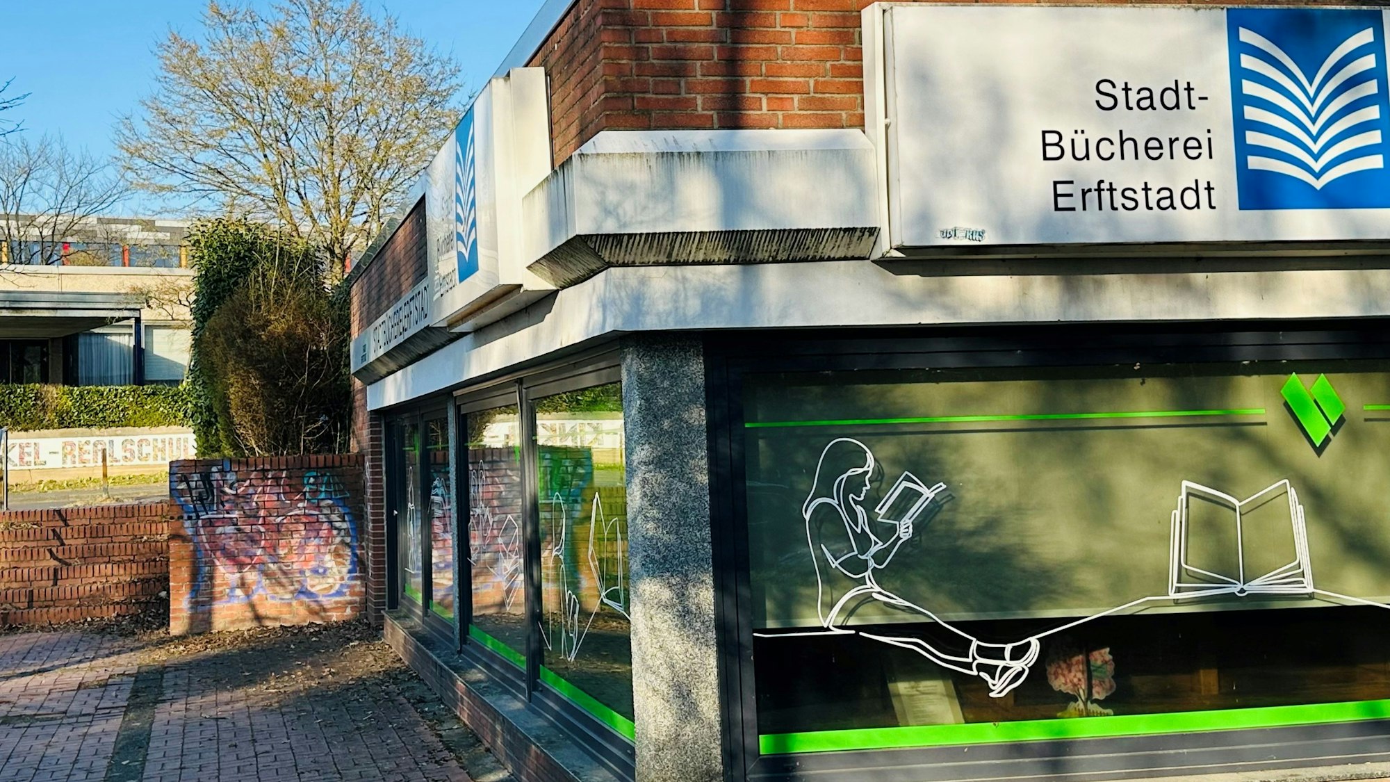 Zu sehen ist ein Gebäude aus Backstein mit einer großen Fensterfront vor blauem Himmel.