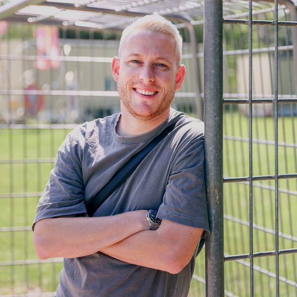 Ein Mann mit blonder Kurzhaarfrisur lehnt an einem Fußballtor in einer Grünanlage.