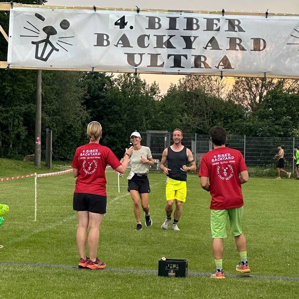 Christine Becker und Markus Habermann laufen nebeneinander ins Ziel, wo ein Mann und eine Frau in Biber-Backyard-T-Shirts warten.