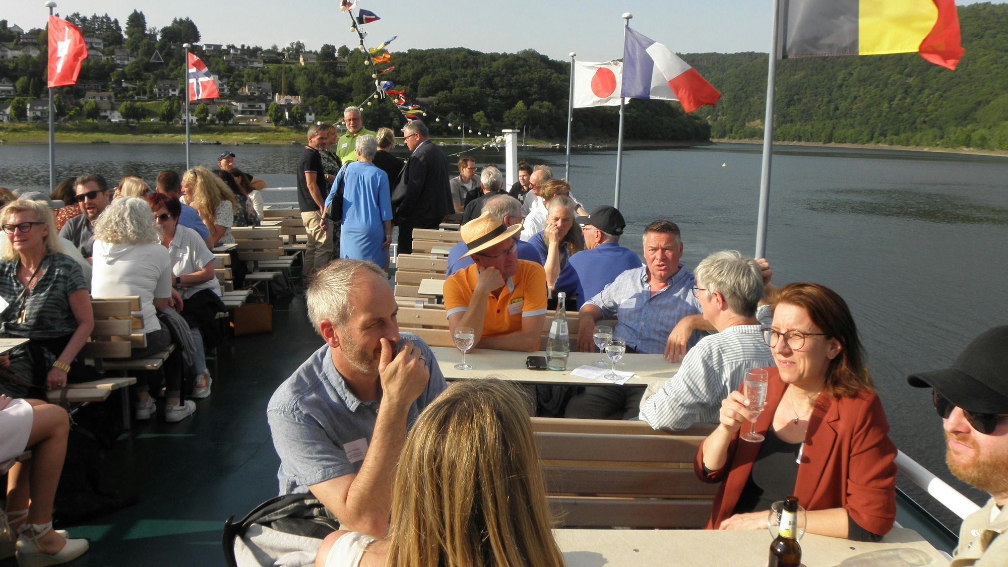 Die Teilnehmer sitzen an den Außentischen an Deck eines Rursee-Ausflugsschiffs.