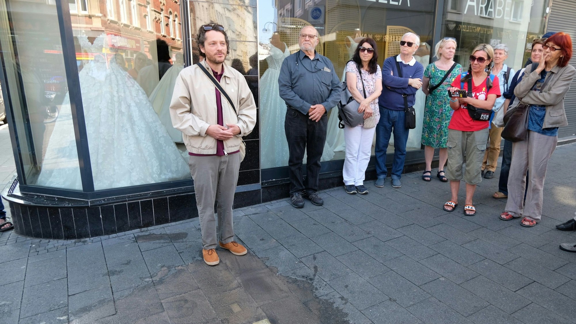 Mehrere Menschen stehen vor einem Schaufenster mit Brautmoden, im Pflaster vor dem Geschäft sind zwei brandneue Stolpersteine verlegt worden.