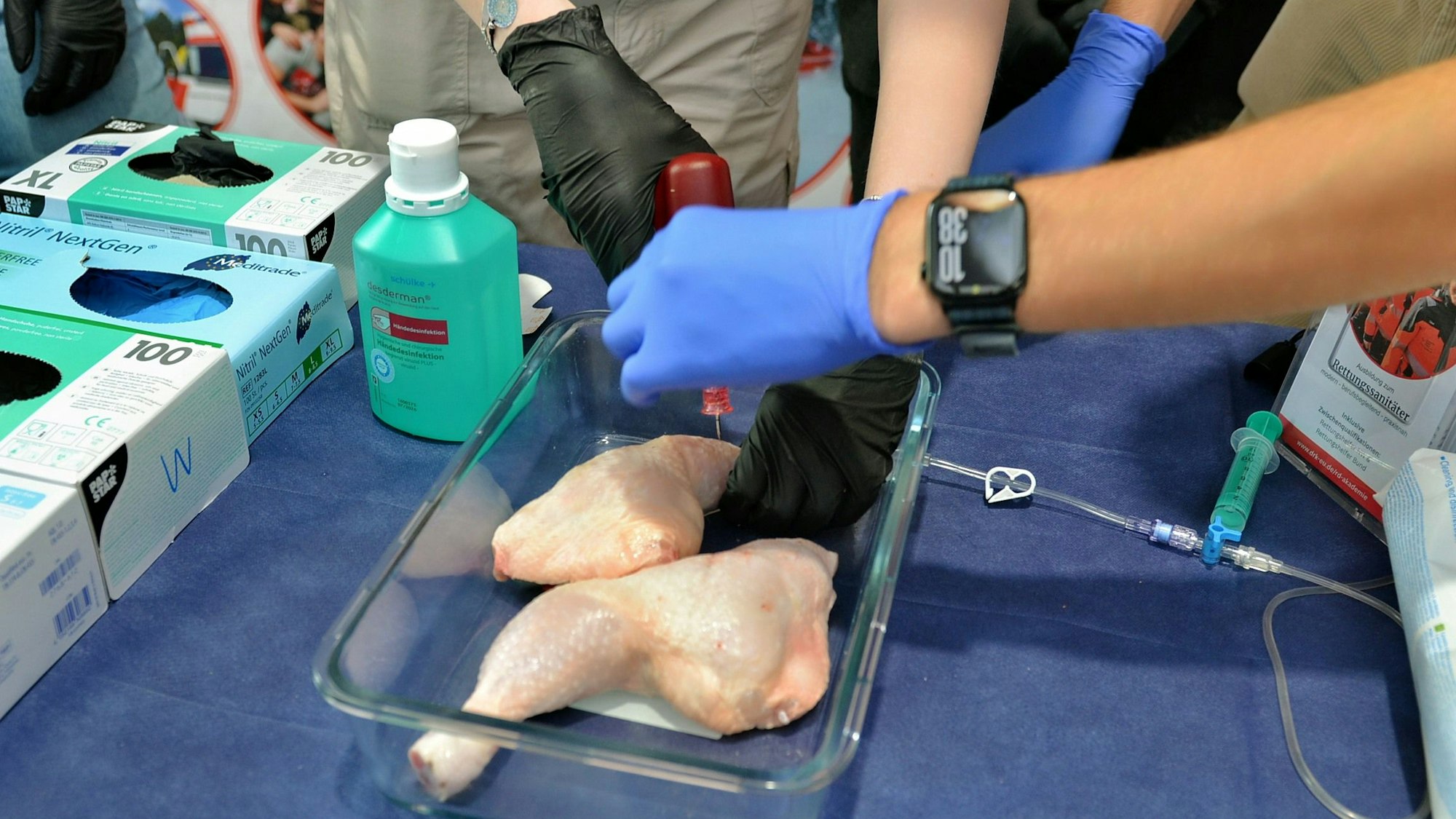 Das Bild zeigt zwei Hähnchenschenkel in einem Behälter. Personen, von denen man nur Arme und Hände sieht, bearbeiten sie mit einem medizinischen Gerät.