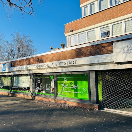 Zu sehen ist ein Gebäude aus Backstein mit einer großen Fensterfront vor blauem Himmel.