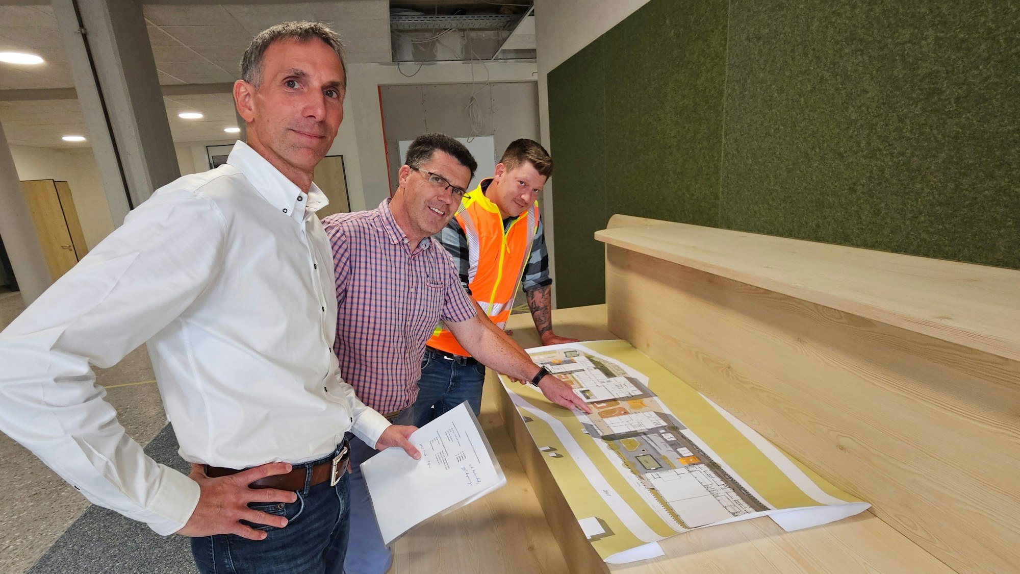 Marcel Wolter (v.l.), Armin Fischbach und Felix Stoff stehen hintereinander und haben vor sich Pläne liegen.