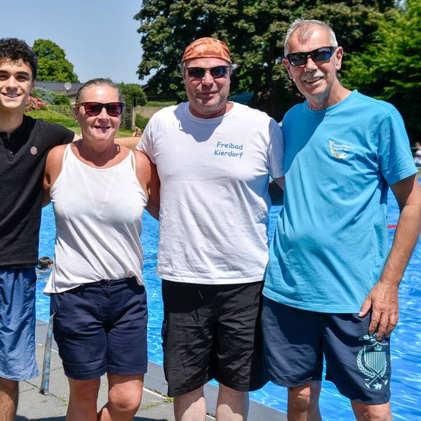 Vier Menschen stehen vor einem Schwimmbecken in Freien.