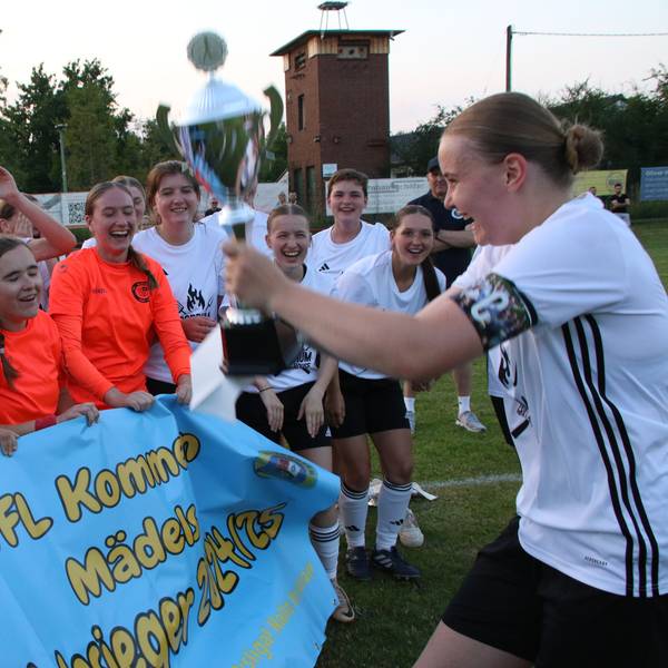 Kapitänin Nele Wagner hält den Pokal in die Höhe und zeigt ihn ihren jubelnden Mitspielerinnen.
