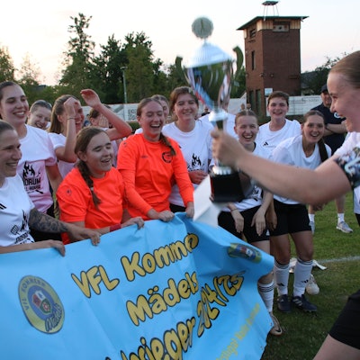 Kapitänin Nele Wagner hält den Pokal in die Höhe und zeigt ihn ihren jubelnden Mitspielerinnen.