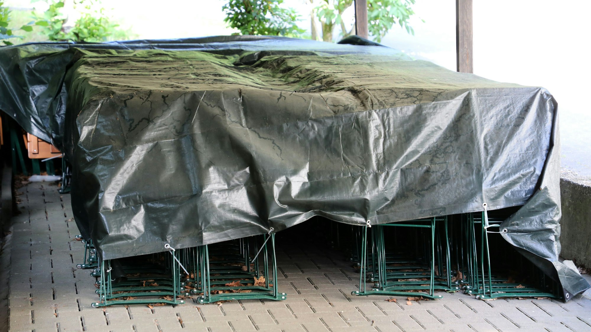 Unter Planen stehen Stühle und Tische der Waldwirtschaft Forsbacher Mühle.