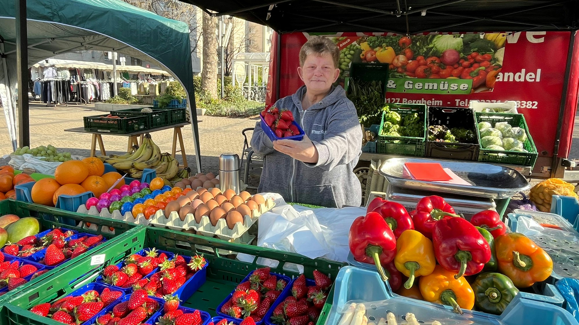 Eine Frau steht hinter ein Marktstand für Obst und Gemüse.