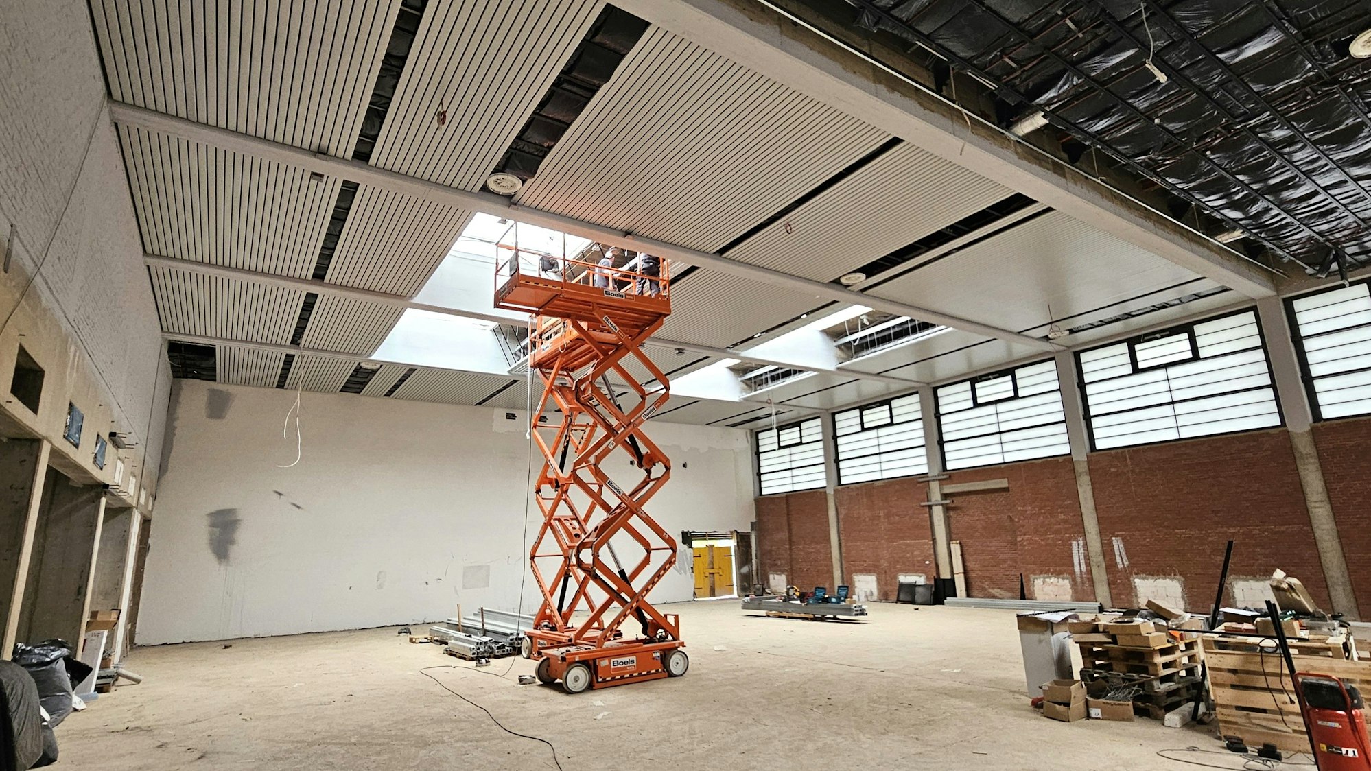 In der Turnhalle steht ein großer Hubwagen, von dem aus an der Decke gearbeitet wird.