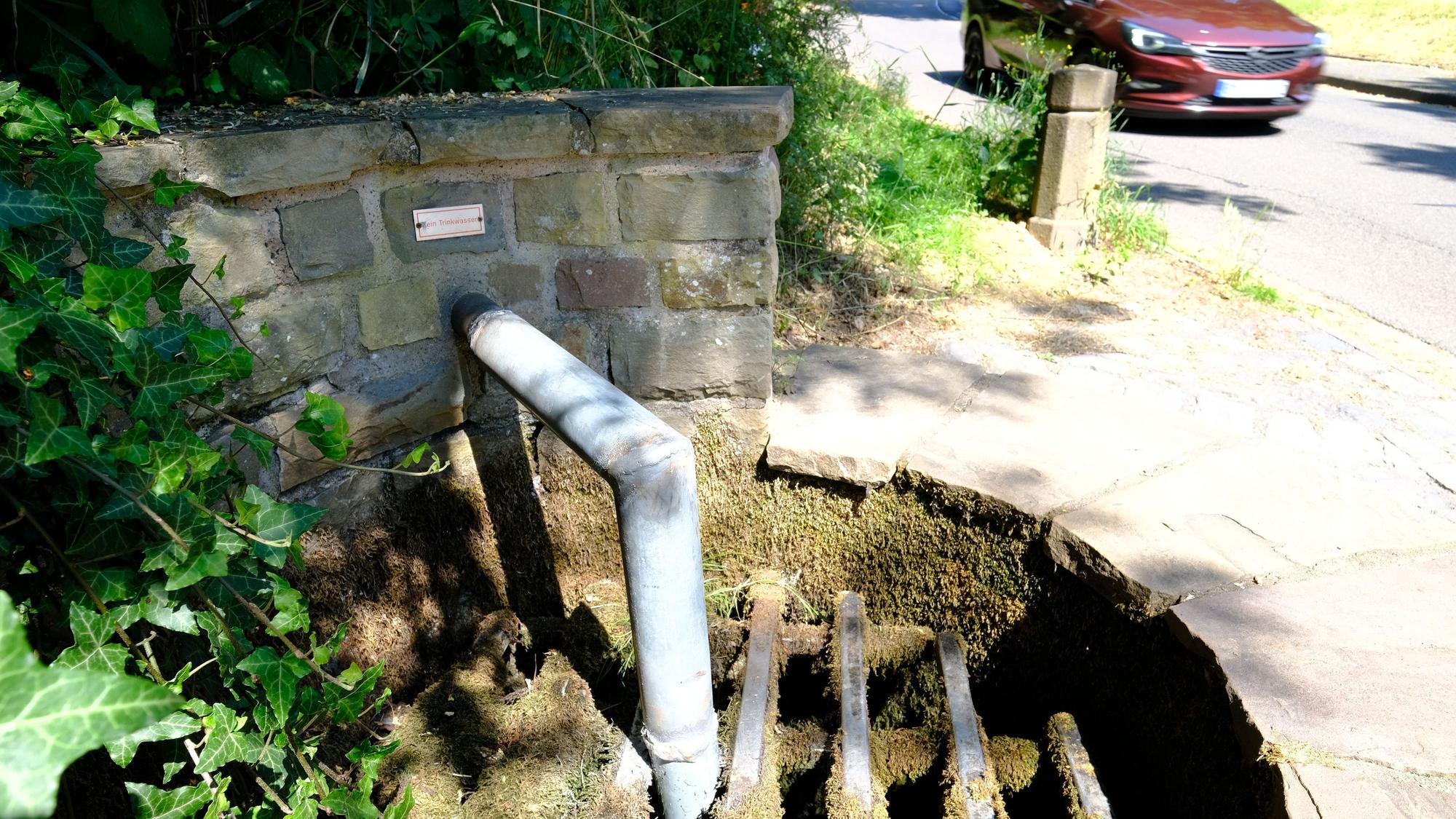 An einem Brunnen ist das Auslassrohr des Wassers bis unter ein Gitter verlängert worden, um die Wasserentnahme zu verhindern.