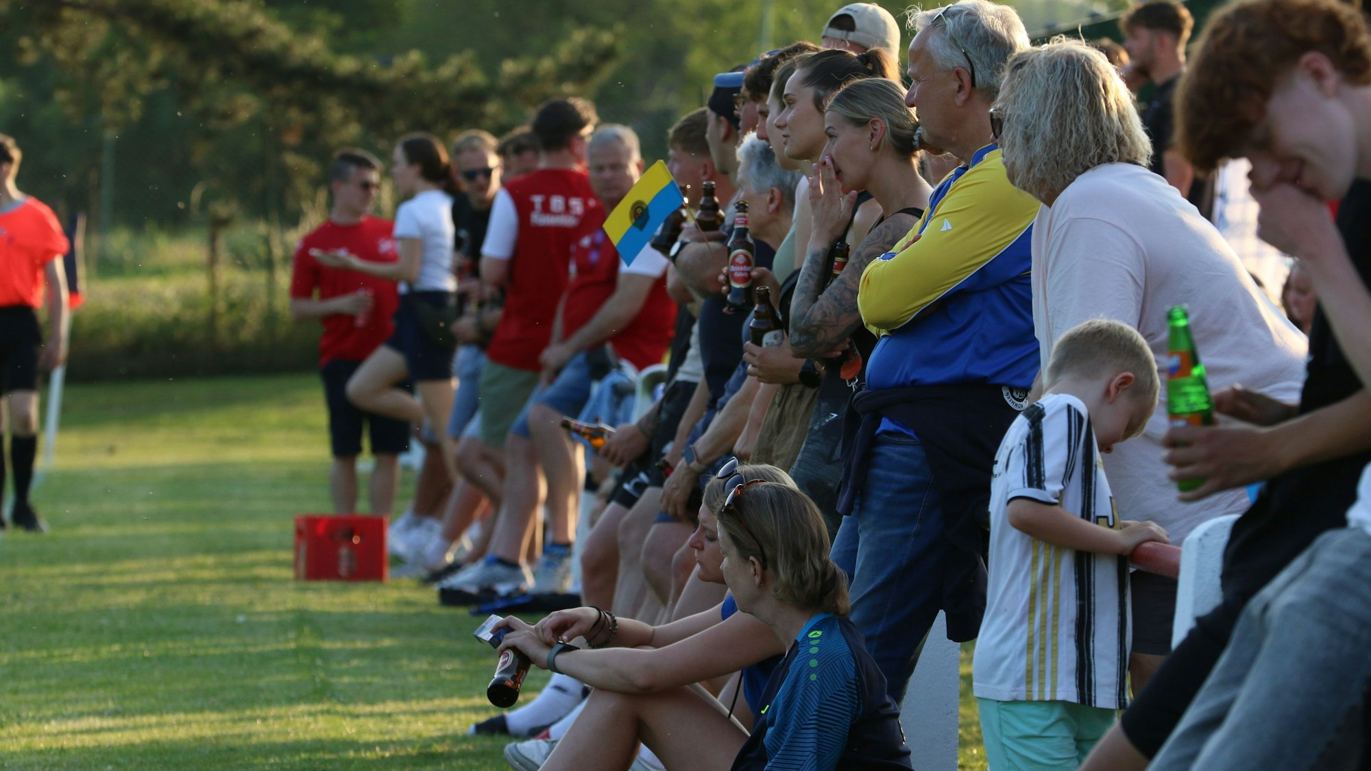 Zuschauer stehen und sitzen am Rande des Spielfeldes und verfolgen das Kreispokalfinale.
