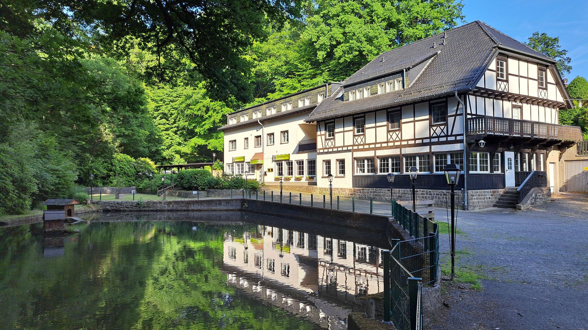 An einem Teich im Wald liegt die Forsbacher Mühle verlassen in der Sonne.