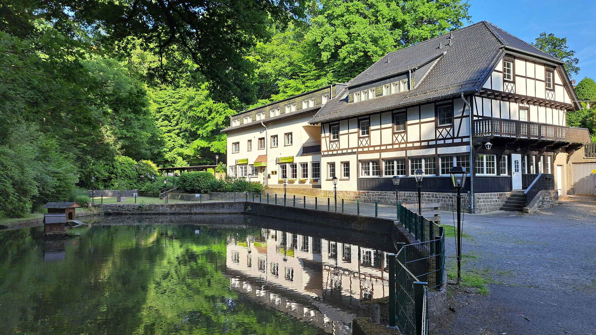 An einem Teich im Wald liegt die Forsbacher Mühle verlassen in der Sonne.