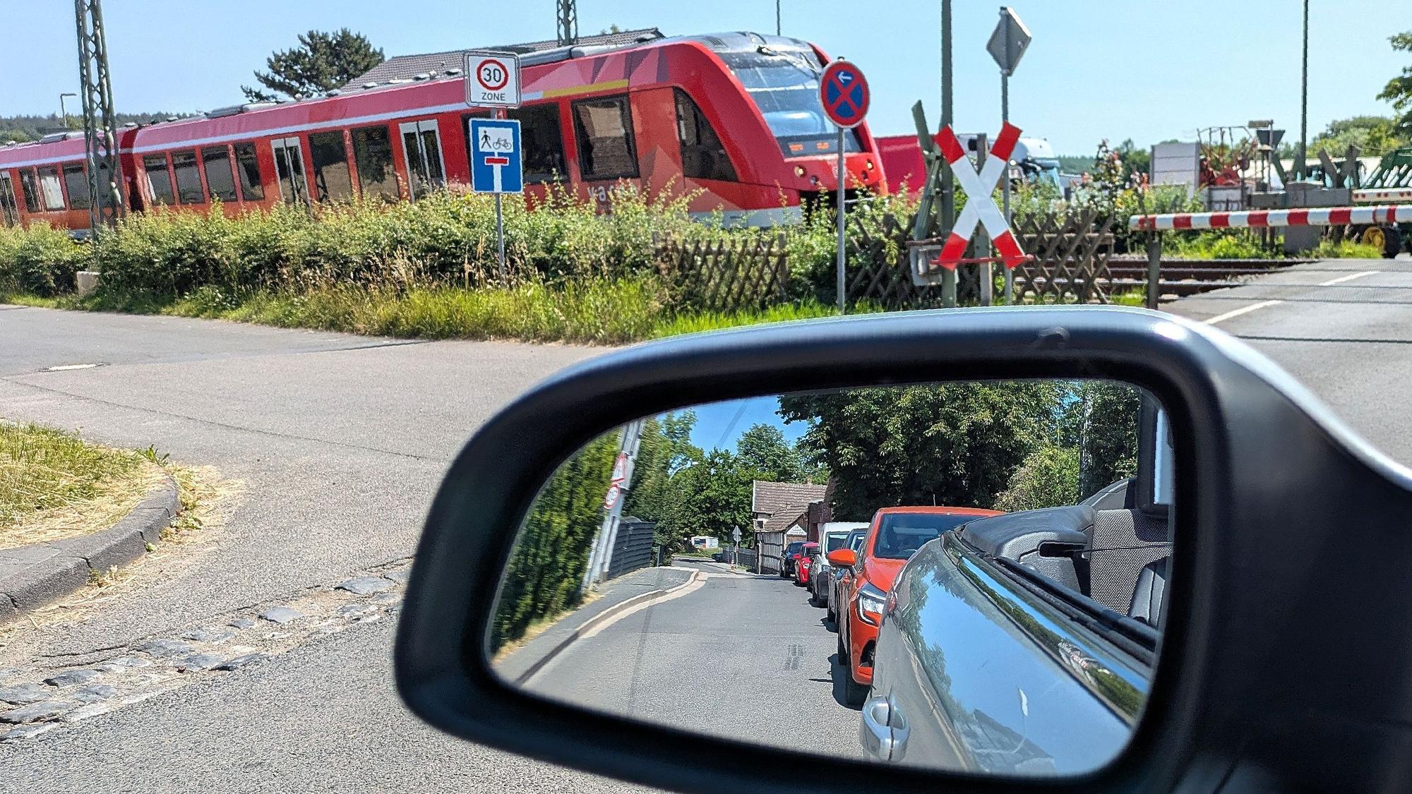 Am Bahnübergang in Satzvey fährt ein Regionalzug in Richtung Mechernich, in einem Auto-Rückspiegel sind wartende Fahrzeuge zu sehen