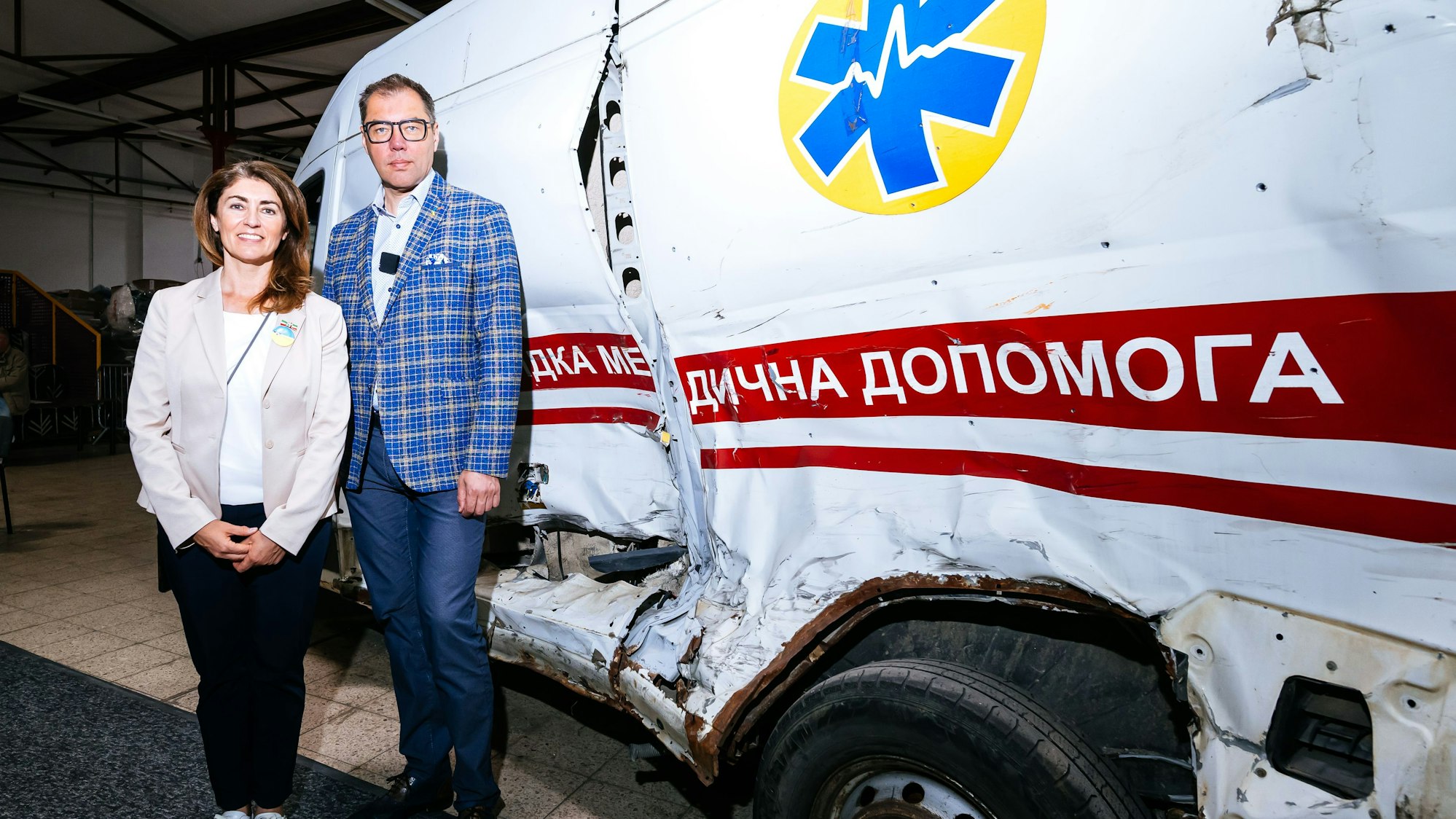 Vor einem zerstörten Rettungswagen: Linda Mai und der Botschafter der Ukraine, Oleksij Makejew.