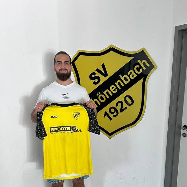 Louis Vedder steht mit dem Schönenbacher Trikot in der Hand vor dem Vereinsabzeichen.