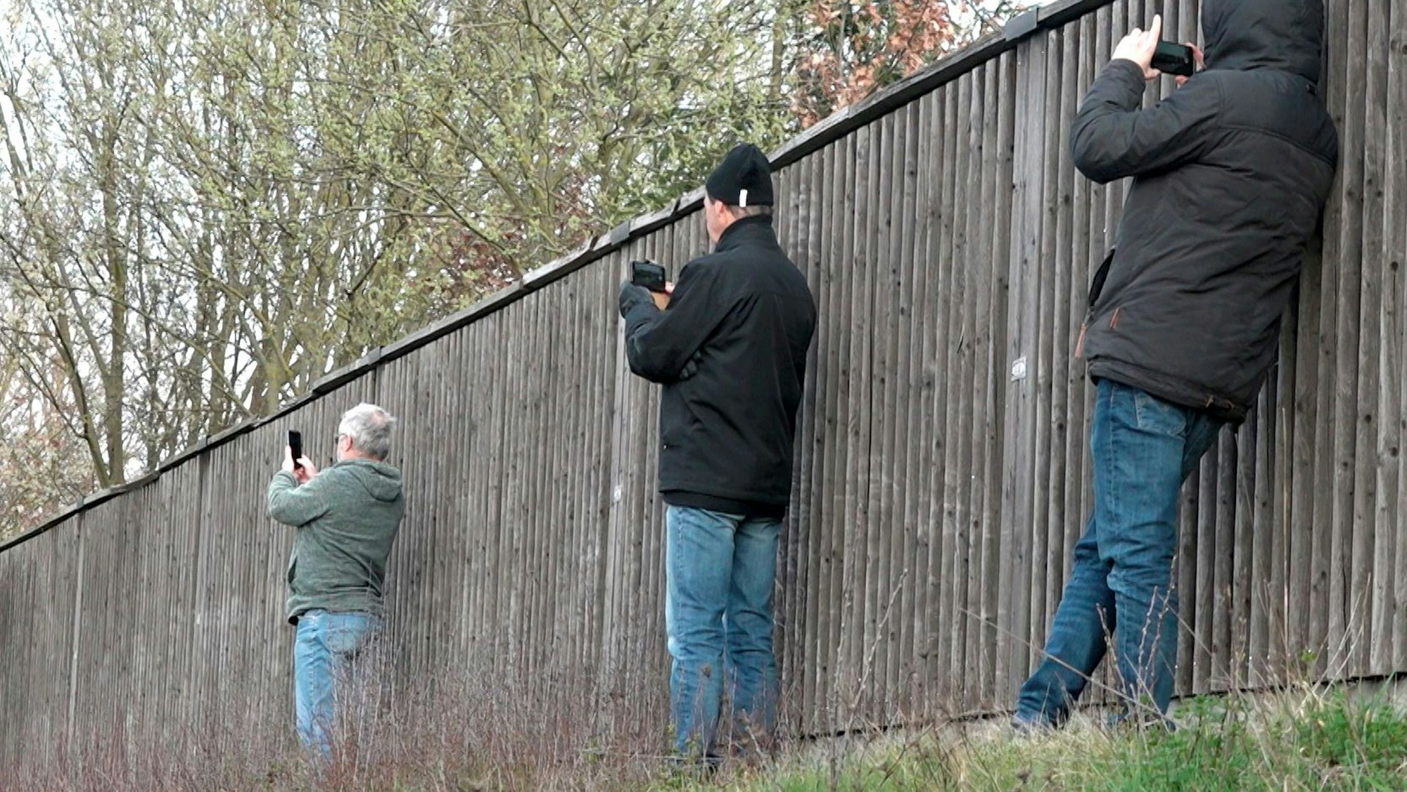 Schaulustige fotografieren neben einer Lärmschutzwand mit ihren Smartphones eine Unfallstelle.